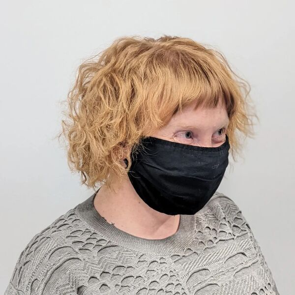 French Curly Bob - a woman wearing a gray blouse and a mask
