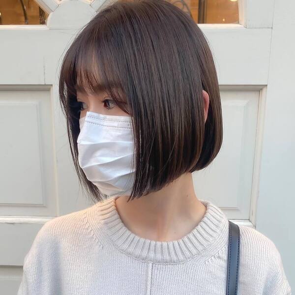Milky Bob Japanese Hairstyles for Women - a woman wearing mask and knitted sweater with sling bag.