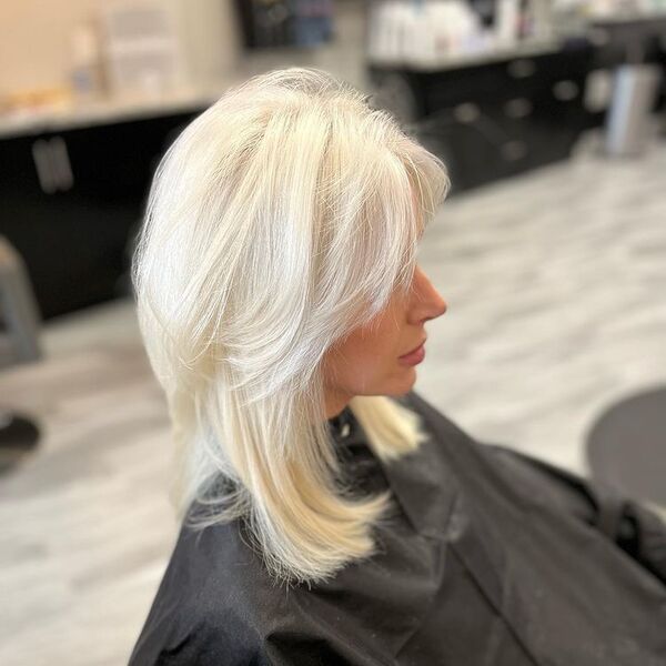 Platinum White Blonde with Curtain Bangs - a woman wearing a black salon cape