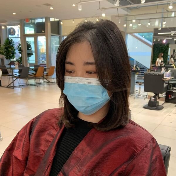 A woman wearing a blue mask and silky red salon cape with her layered bob wash and go hairstyles
